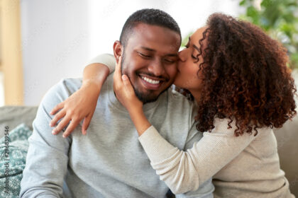 love, valentines day and relationships concept - happy african american couple sitting on sofa at home and kissing